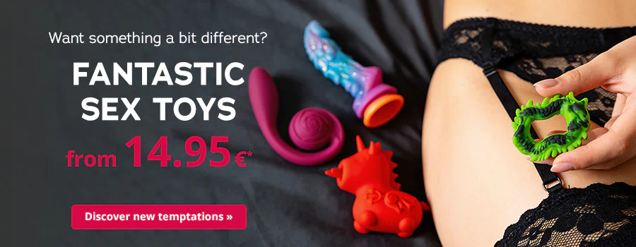 A person is wearing black lace lingerie and holding a green toy in their hand. There is a red and a pink toy lying next the the person on a dark piece of fabric. The text says: "Want something a bit different?", "Fantastic toys from 14.95€*" and "Discover new temptations »".