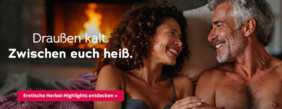 Ein Paar liegt dicht zusammen im Bett und lächelt sich an. Links eine Frau im Spitzen-BH und dunklen Locken, rechts ein oberkörperfreier Mann, mit grauem Haar und Bart. Text: „Draußen kalt. Zwischen euch heiß.“ Roter Button: „Erotische Herbst-Highlights entdecken“.