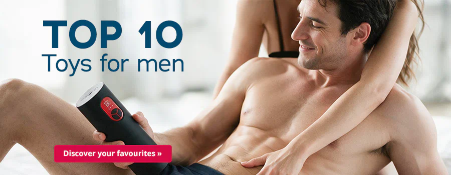 A man is lying on a bed in black underwear. He is topless and he is holding a black masturbator in his hand. A woman is sitting behind him, running her hand over his stomach and hips. The image has some text that says: “TOP 10 Toys for Men” and “Discover your favourites »”.