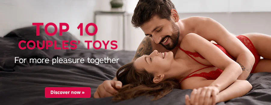 A couple is lying on a bed with dark bedding. They are smiling at each other. The woman is wearing red lace lingerie. The man is lying half on top of her and embracing her. Thee is some large text that says: “Top 10 Couples' Toys – For more pleasure together”. There is a red button at the bottom with some white text that says: “Discover now”.