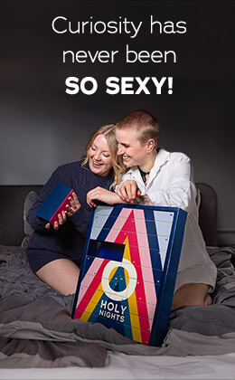 The advertisement has a picture of two women kneeling on a bed and looking at a box of the Advent calendar together. The calendar has a colourful design and the words "HOLY NIGHTS" are written on it. The sentence "Curiosity has never been so sexy!" is written next to it in white letters.