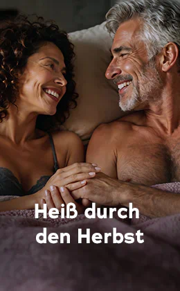 Ein Paar liegt dicht zusammen im Bett und lächelt sich an. Links eine Frau im Spitzen-BH und dunklen Locken, rechts ein oberkörperfreier Mann, mit grauem Haar und Bart. Text: „Heiß durch den Herbst.“ Roter Button: „Entdeckt Lust-Booster."