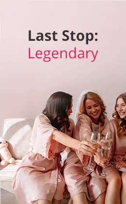 Several women in pink satin dressing gowns are sitting next to each other on a light sofa and clinking champagne glasses. One of them is wearing a white veil. There is a beige plush toy in the background. There is some text at the top that says: “Last Stop: Legendary”. There is a red button at the bottom with the text: “Start your hen party now.”