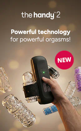 A hand is holding a black masturbator in front of a beige background. Several transparent attachments can be seen in the background. The words “the handy 2” and “Powerful technology for powerful orgasms!” can be seen at the top. There is a red circle next to the masturbator with the word “NEW” written on it.